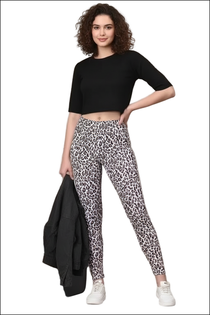 Woman in a black short-sleeve crop top, pink leopard print leggings, holding a black jacket, with white sneakers.