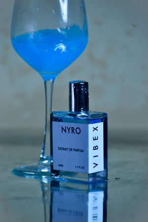 Nyro VIBEX Extrait de Parfum bottle next to a blue cocktail glass on a reflective surface