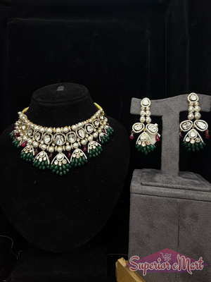 Ornate gold-toned jewelry set with white stones, pearls, and green and red bead accents on dark display stands.