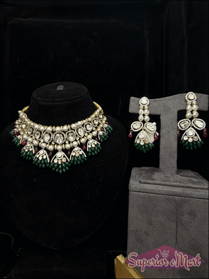 Ornate gold-toned jewelry set with white stones, pearls, and green and red bead accents on dark display stands.