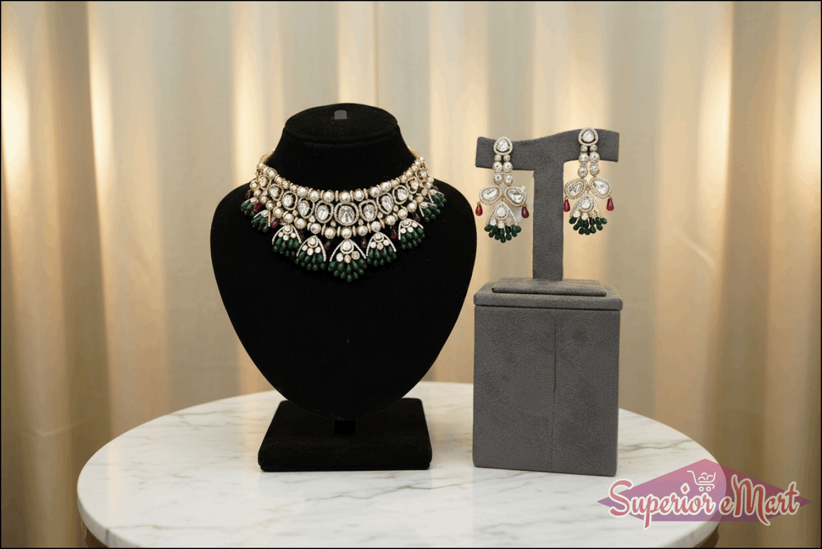 Ornate gold necklace and earring set with diamonds, green emerald beads, and red rubies on velvet display stands.