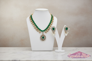 Gold emerald and diamond necklace with matching pearl-drop earrings on white jewelry displays.