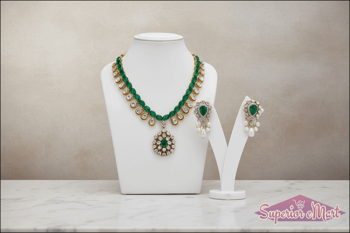 Gold emerald and diamond necklace with matching pearl-drop earrings on white jewelry displays.