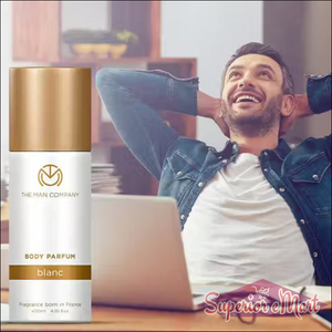 White and gold The Man Company Blanc Body Parfum bottle. Background: a man smiling and relaxing at a laptop.