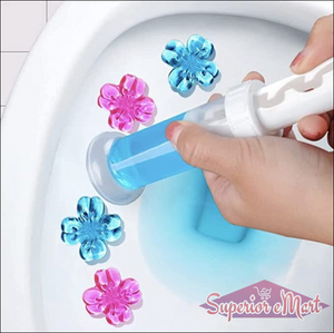 Blue and pink flower-shaped gel toilet stamps being applied to a white bowl with a hand-held plastic applicator.
