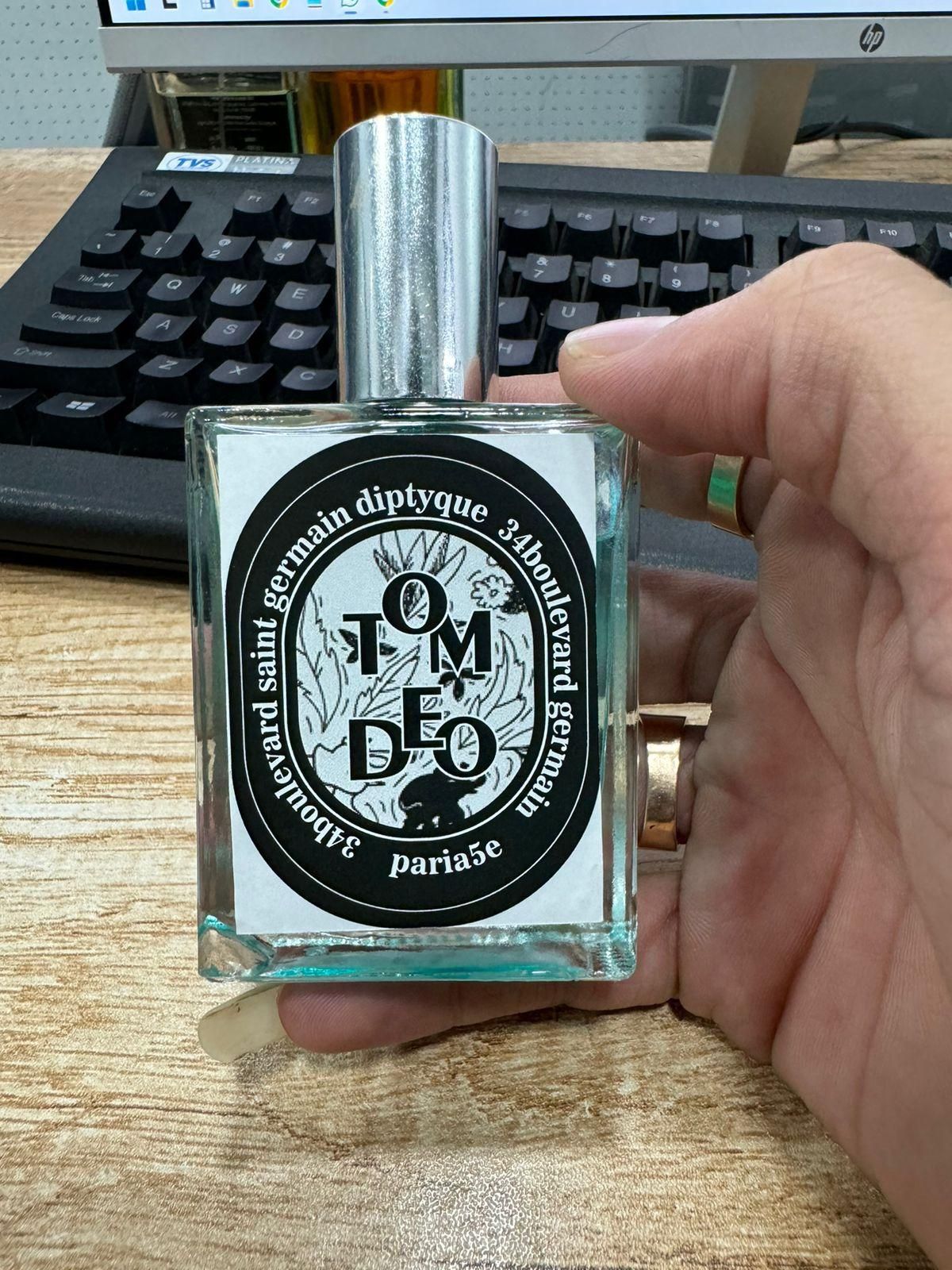Hand holding a 34 Boulevard Germain perfume bottle with black and white label on wooden desk near computer keyboard