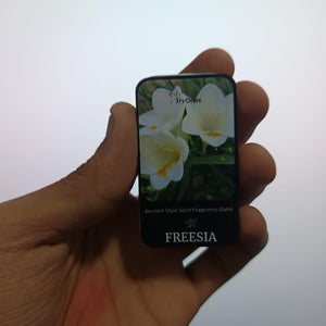 Hand holding ancient style solid perfume in freesia scent with floral packaging design