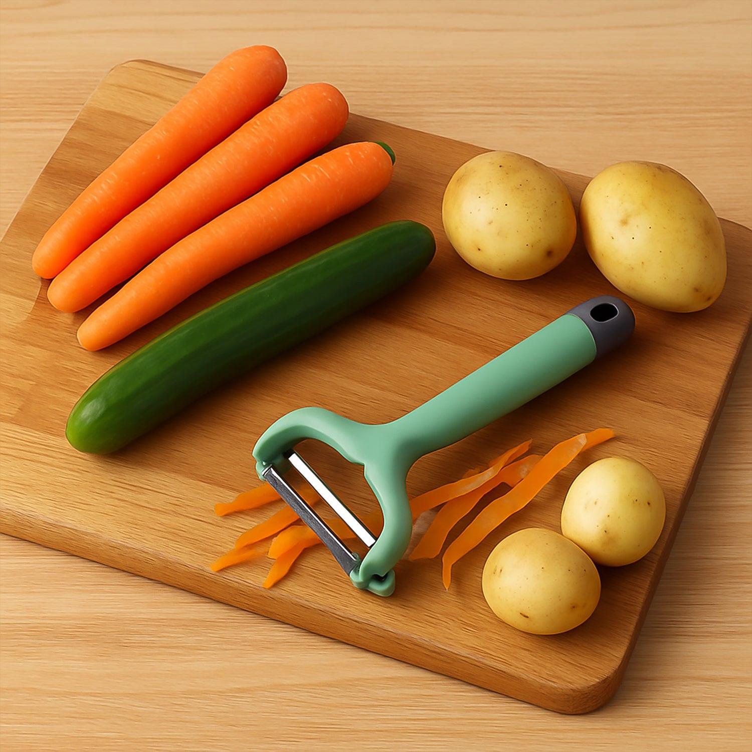 Vegetable fruit peeler in green next to fresh carrots, potatoes, and cucumber on a wooden cutting board