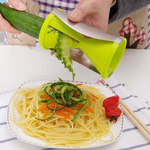 Hands using a vegetable spiralizer slicer to create zucchini noodles over a plate of pasta