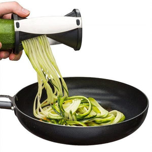 Handheld vegetable spiralizer slicer creating zucchini noodles in a frying pan