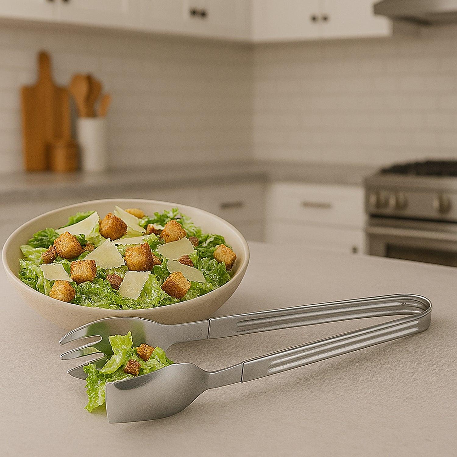 2-in-1 stainless steel serving tong set with salad in a bowl on a kitchen countertop