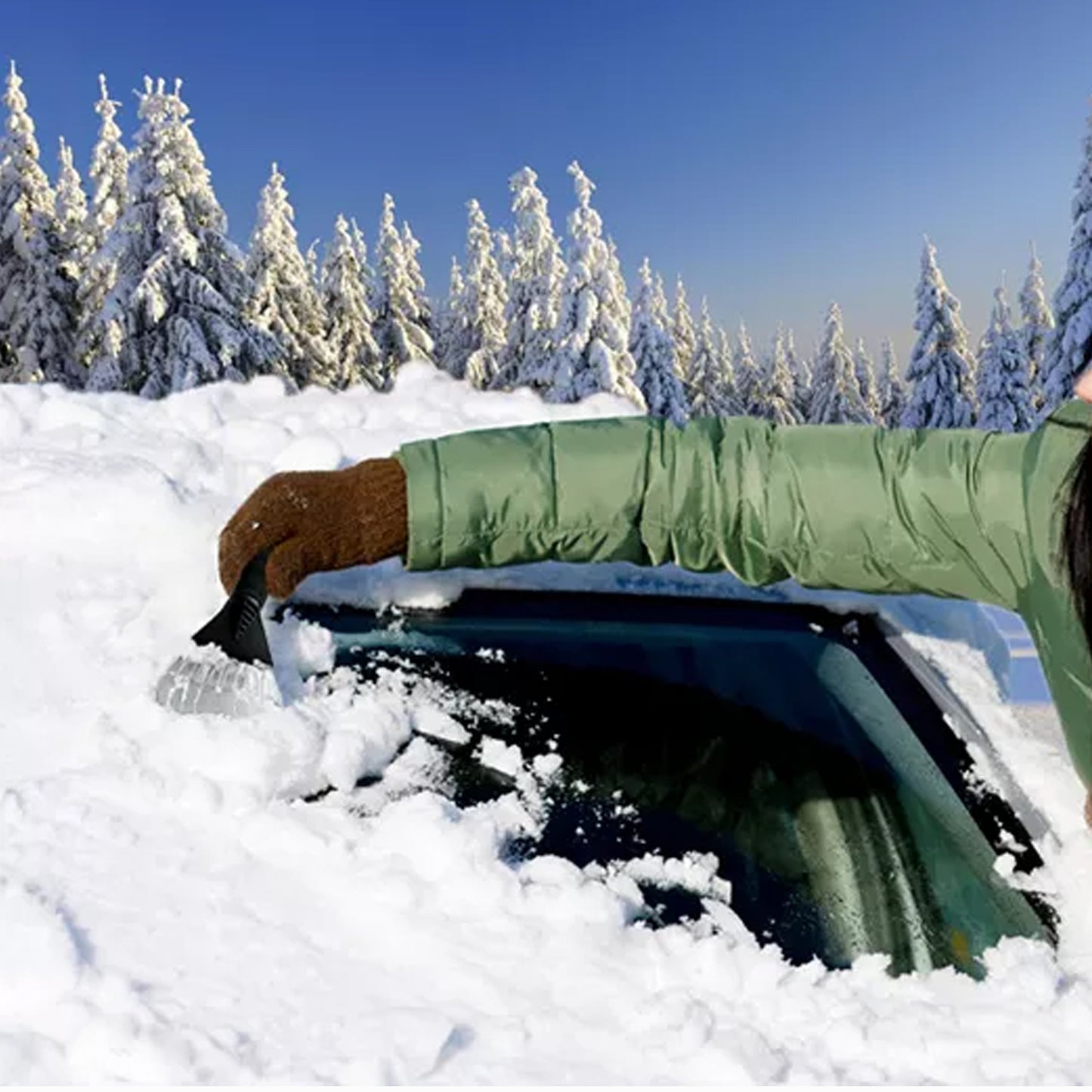 User using a windshield ice scraper tool to remove snow from a car windshield in a snowy landscape