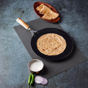 Wooden handle roti tawa on a kitchen countertop with freshly made roti and sides