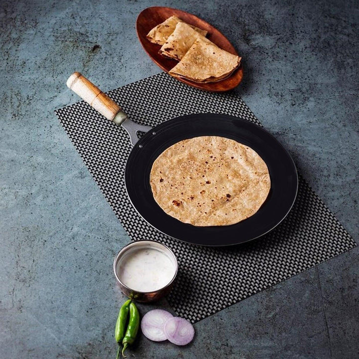 Wooden handle roti tawa on a kitchen countertop with freshly made roti and sides
