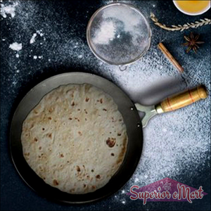 Wooden handle roti tawa with a perfectly cooked roti on a kitchen counter sprinkled with flour